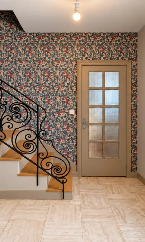 Pose de papier peint décoratif à motifs végétaux dans une entrée avec escalier en bois